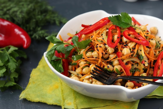 Insalata salutare di ceci, carote coreane, peperoni e cipolle decorata con sesamo nero e prezzemolo