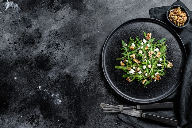 Insalata sana con rucola, formaggio di capra, noci e salsa vinaigrette. Sfondo nero