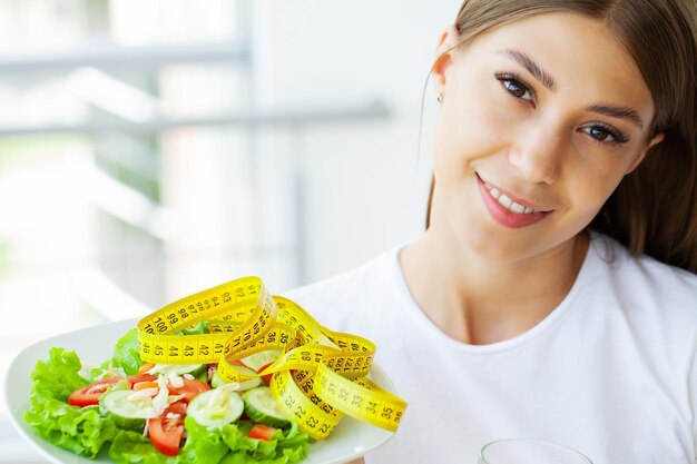 Insalata sana della tenuta della giovane donna con ingredienti freschi verdi e nastro adesivo giallo.