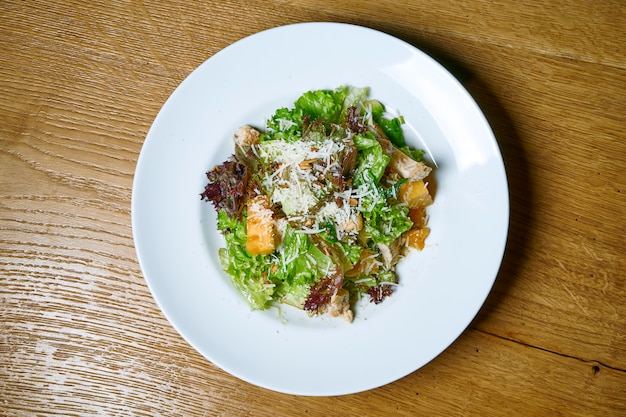 Insalata saporita e fresca con lattuga, parmigiano e tacchino al forno su un piatto bianco su una tavola di legno. Cibo vista dall'alto. Nutrizione Sana