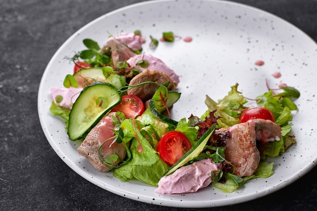 Insalata tiepida con vitello e crema di formaggio, su un piatto bianco e un tavolo scuro