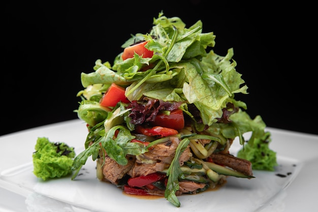 Insalata tiepida di vitello, su un piatto bianco, su sfondo nero. vista laterale