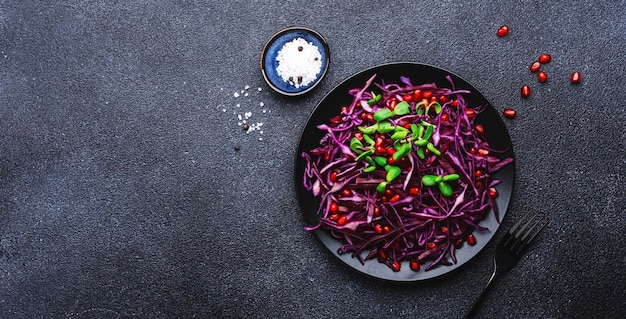 Insalata vegana con cavolo rosso prezzemolo semi di melograno germogli di girasole e condimento all'olio d'oliva su sfondo nero tavolo da cucina vista dall'alto banner