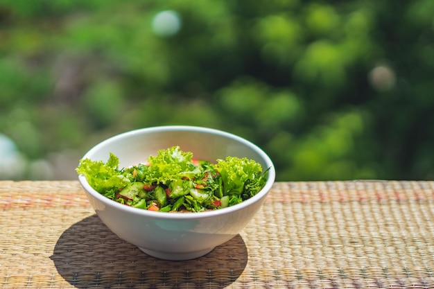 Insalata vegana cruda con foglie verdi mescolare le verdure in una ciotola bianca Ricetta di cucina pomodoro misto carota prezzemolo coriandolo aneto verde cetriolo basilico peperone Cibo sano vitamine per l'immunità