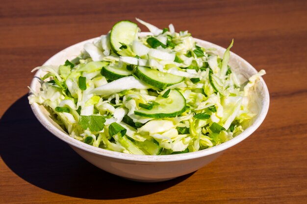 Insalata vegana di primavera con cavolo, cetriolo, cipolla verde e prezzemolo su un tavolo di legno