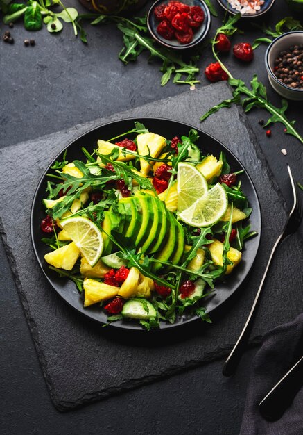 Insalata vegana fresca con avocado di rucola di ananas e mirtillo rosso essiccato su pietra nera vista dall'alto del tavolo da cucina Mangiare sano dieta pulita cibo concetto di perdita di peso