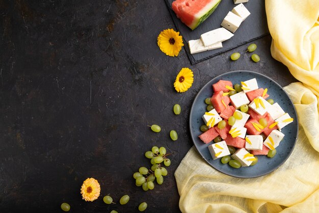 Insalata vegetariana con anguria, formaggio feta e uva sul piatto in ceramica blu