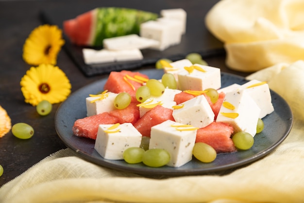 Insalata vegetariana con anguria, formaggio feta e uva sul piatto in ceramica blu