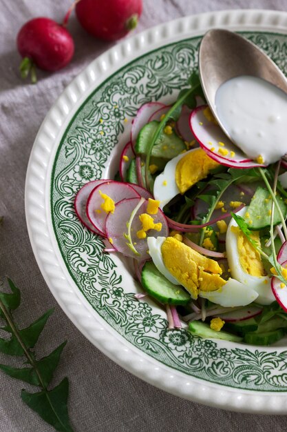 Insalata vegetariana con foglie di tarassaco, verdure, uova e panna acida. Stile rustico.