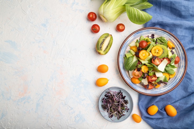 Insalata vegetariana di pac choi cavolo, kiwi, pomodori, kumquat, germogli microgreen su una superficie di cemento bianca. Vista dall'alto, copia spazio.