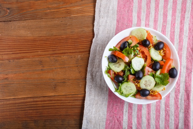 Insalata vegetariana di pomodori, cetrioli, prezzemolo, olive e senape sulla tovaglia di lino.