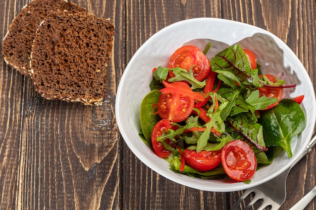 Insalata vegetariana di pomodorini, spinaci, cipolle rosse e peperoni con burro. Su uno sfondo di legno. Copia spazio.