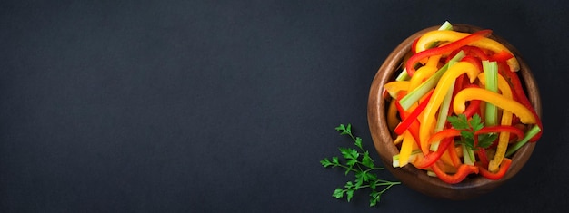 Insalata vegetariana di sedano, peperoni rossi e gialli in una ciotola di bambù su uno sfondo scuro.Vista dall'alto. Spazio per il testo. Messa a fuoco selettiva.