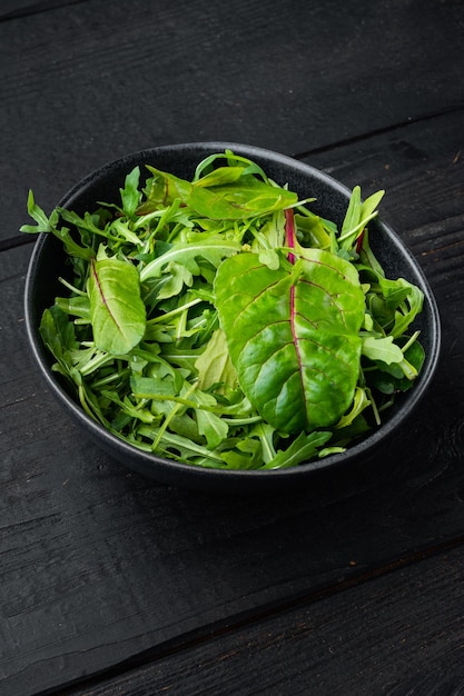 Insalata verde alle erbe con rucola e bietole Mangold su sfondo nero tavolo in legno