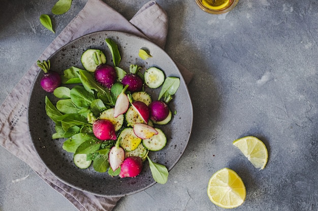 Insalata verde con rucola, cetriolo, ravanello, lime, olio d'oliva, erbe aromatiche scottate su sfondo grigio pietra