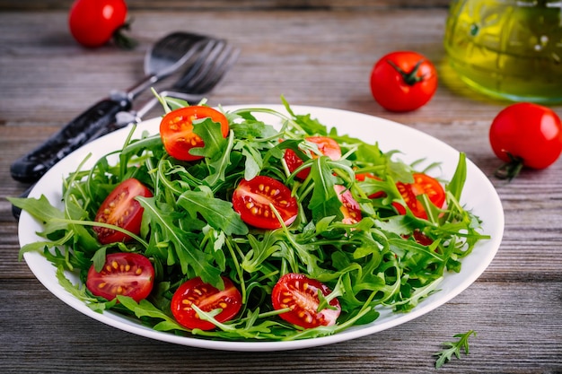 Insalata verde fresca con rucola e pomodori rossi su fondo di legno rustico