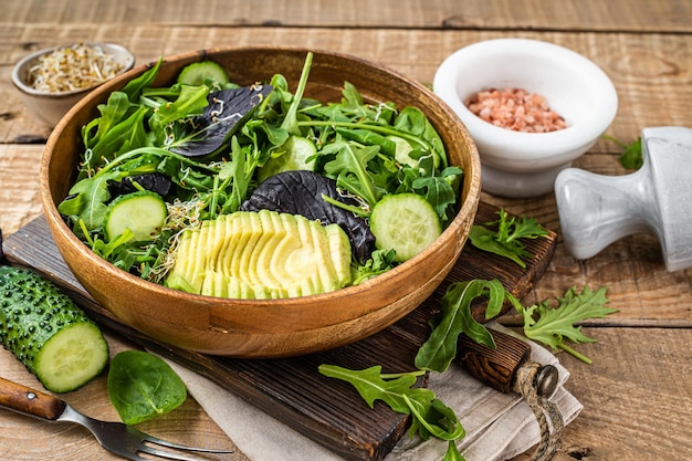 Insalata verde vegana con mix di foglie verdi, avocado e verdure. Fondo in legno. Vista dall'alto.