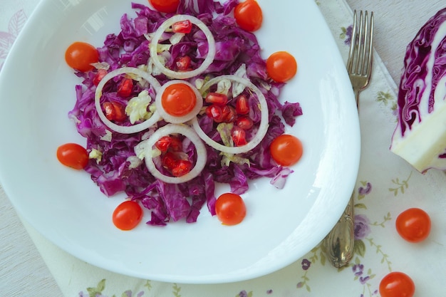 Insalata vitaminica in un piatto bianco triangolare: cavolo viola con pomodorini, cipolla, foglie di insalata, chicchi di melograno, succo di limone e olio d'oliva. Sfondo. Vista dall'alto.