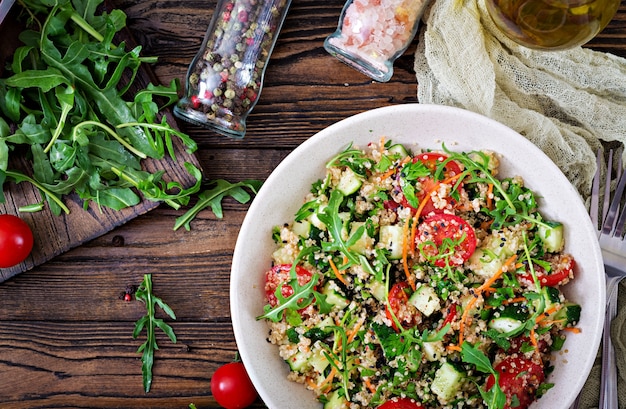 Insalate con quinoa, rucola, ravanello, pomodori e cetriolo in ciotola sul tavolo di legno. Cibo sano, dieta, disintossicazione e concetto vegetariano. Vista dall'alto. Disteso