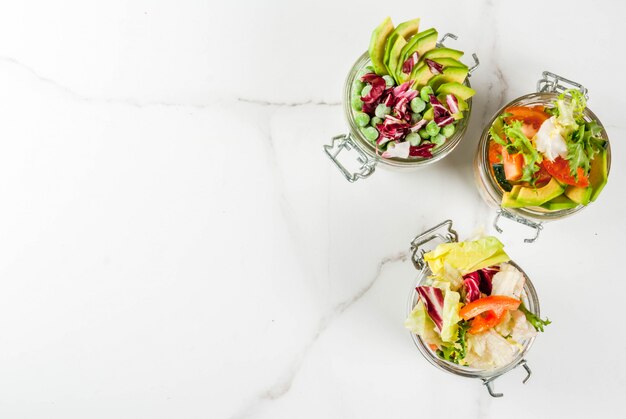 Insalate fresche in barattolo con verdure fresche e condimenti sani, sul tavolo di marmo bianco,