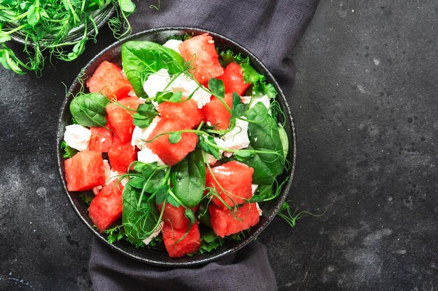 Insalatiera di anguria con spinaci al formaggio di capra e germogli di pisello su sfondo grigio vista dall'alto spazio copia