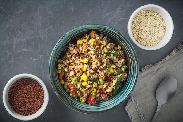 Insalatiera di quinoa con verdure: carota, mais, peperone, piselli e due ciotole con quinoa rossa e bianca