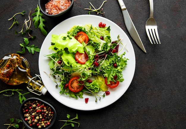 Insalatiera mista verde fresca con pomodori e microgreens sul tavolo di cemento nero. Cibo sano, vista dall'alto.