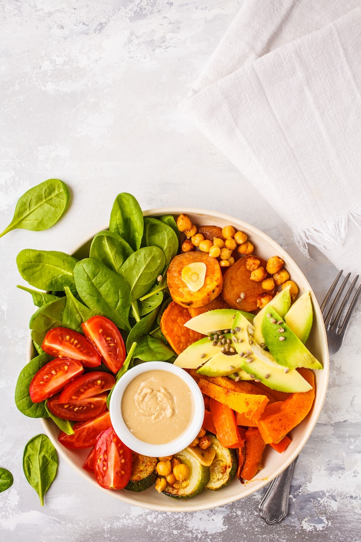 Foto insalatiera vegan con verdure al forno, ceci, avocado e tahini vestirsi su uno sfondo bianco