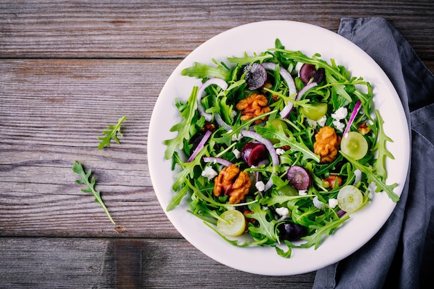 Insalatiera verde con noci di rucola formaggio di capra cipolla rossa e uva su fondo di legno