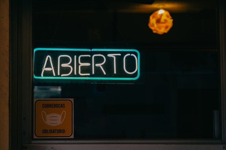 Insegna aperta in lettere al neon e uso obbligatorio di maschere per il viso in spagnolo.