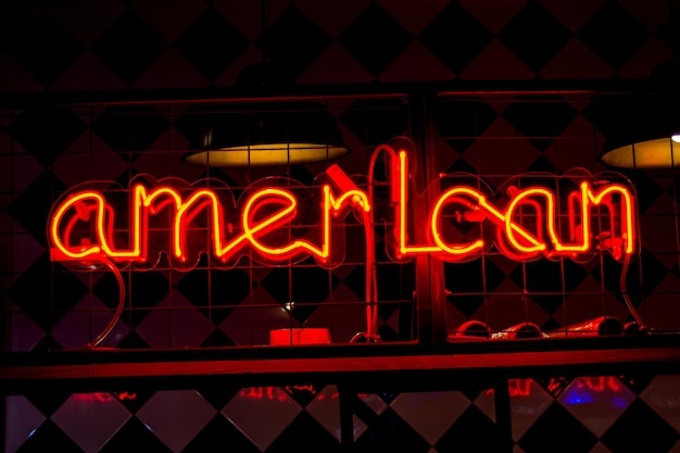 Insegna rossa al neon luminosa AMERICANA e luci sfocate su sfondo nero. Immagine vintage toni scuri.