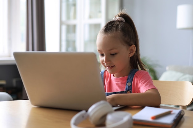Insegnamento a distanza. Bambina allegra in cuffia utilizzando il computer portatile che studia tramite il sistema di e-learning online.
