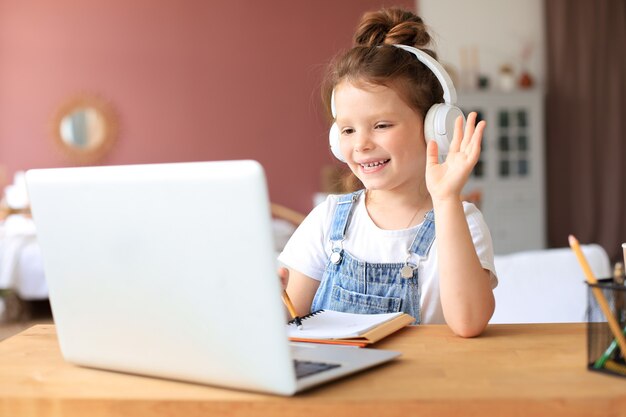 Insegnamento a distanza. Bambina allegra in cuffia utilizzando il computer portatile che studia tramite il sistema di e-learning online.