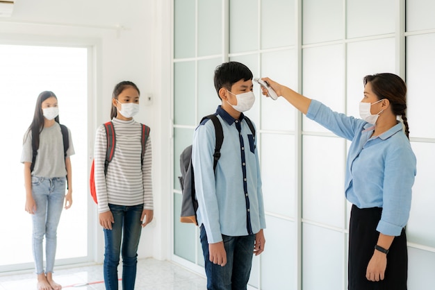 Insegnante asiatico della donna che per mezzo dello studente dello screening della temperatura del termometro per febbre