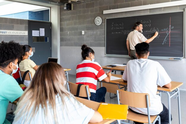 Insegnante bianco uomo maturo scrive formule matematiche sulla lavagna con il gesso. Il gruppo multirazziale di studenti presta attenzione alla spiegazione. copia spazio. Concetto di educazione. Prendi nota