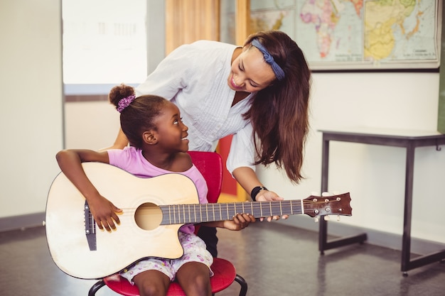 Insegnante che assiste una ragazza a suonare una chitarra in aula