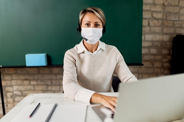 Insegnante con maschera facciale protettiva che utilizza il laptop in classe