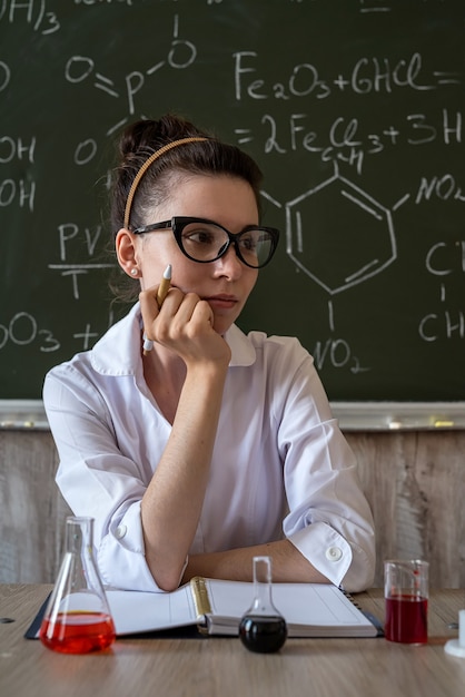 Insegnante di chimica donna mescola liquidi in una boccetta di vetro contro la lavagna con formula chimica