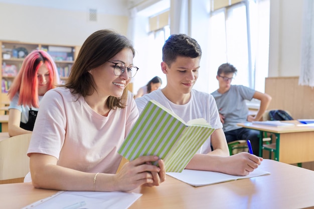 Insegnante di mezza età seduto alla scrivania con uno studente adolescente insegna e verifica la conoscenza. Lezione in classe di bambini di 16 anni, istruzione, adolescenti, concetto di college scolastico