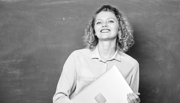 Insegnante di scuola con il taccuino Insegnamento dell'informatica Ritorno a scuola Donna insegnante allegra tenere supporto per laptop vicino alla lavagna Concetto di istruzione scolastica Software per insegnanti Istruzione moderna