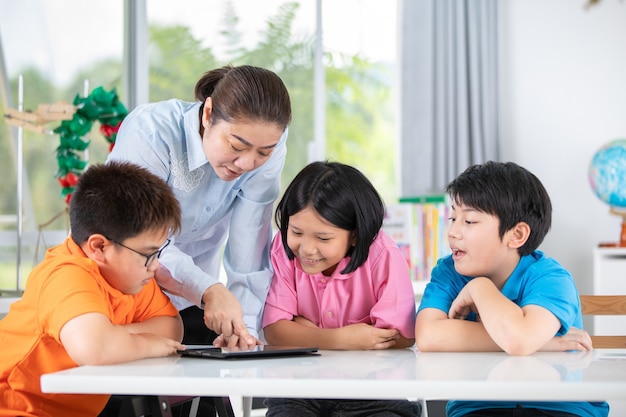 Insegnante e bambini asiatici che si divertono facendo uso della compressa digitale