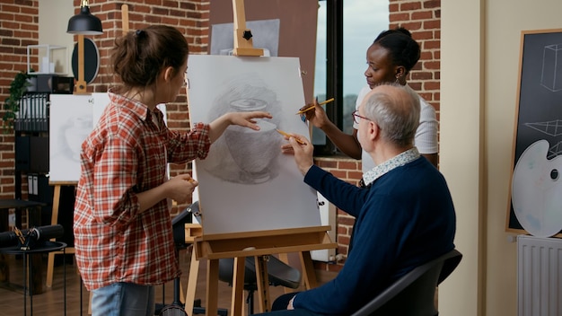 Insegnante e studente che aiutano il vecchio a disegnare un vaso su tela, spiegando le abilità di disegno. Persona anziana che frequenta le lezioni di arte come propositi per il nuovo anno per sviluppare la crescita educativa.