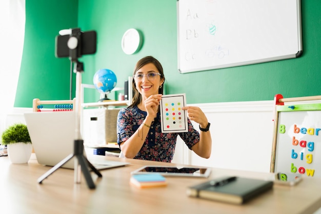 Insegnante femminile attraente che tiene flashcard e insegna i colori ai bambini dell'asilo durante una lezione virtuale