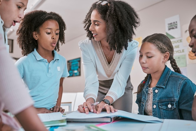 Insegnante femminile che fa allo studente una domanda bambini che imparano in classe e firmano i compiti nel libro Scuola per insegnare educatore che legge quaderno per bambini e gruppo che lavorano insieme per la valutazione