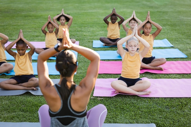 Insegnante femminile e gruppo di diversi studenti che praticano yoga e meditano nel giardino della scuola