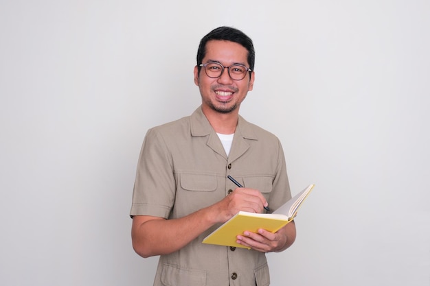 Insegnante indonesiano che sorride felice mentre tiene in mano un libro e una penna