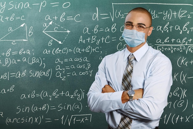 Insegnante maschio con maschera che insegna lezione di matematica a scuola. Distanziamento sociale e classe