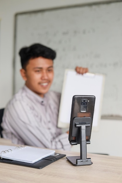 Insegnante o tutor maschio asiatico con lezioni online che insegnano a distanza utilizzando lo smartphone seduto in classe