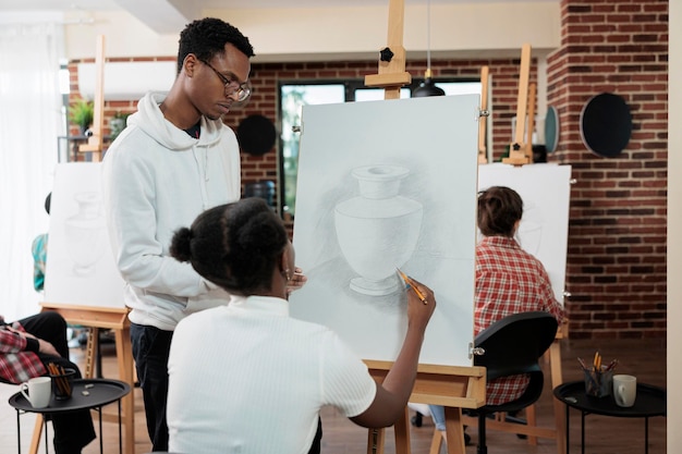 Insegnante pittore che spiega la tecnica dell'illustrazione allo studente che lavora insieme alla tecnica grafica per il progetto scolastico. Gruppo eterogeneo di artisti che disegnano un modello di vaso su tela bianca durante la lezione d'arte