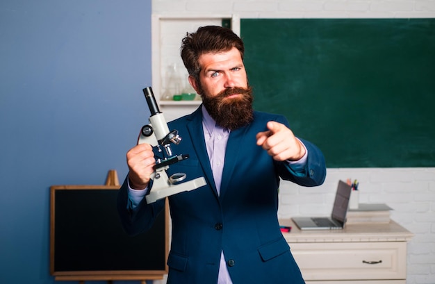 Insegnante uomo barbuto con un notebook portatile che ha un'idea che punta il dito verso di te insegnante stupito in attesa